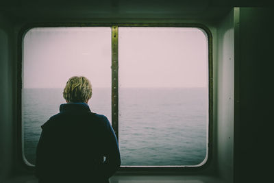Rear view of man looking through window from ship