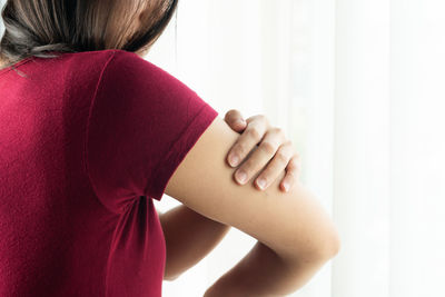 Rear view of woman with arms raised standing against wall