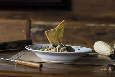 Close-up of bread slice garnished on spaghetti pasta served in bowl on table