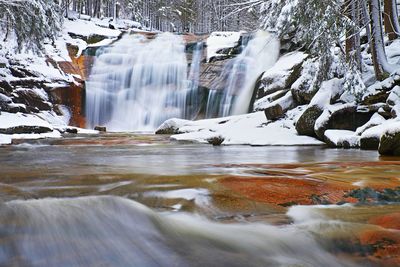 Winter view over snowy boulders to cascade of waterfall. wavy water level.. stream in deep freeze