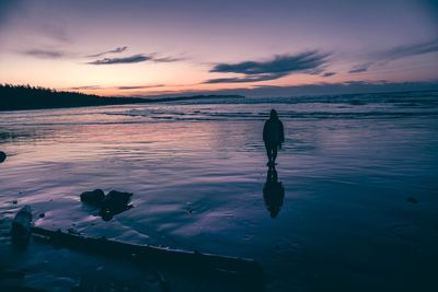 Silhouette person standing in sea against sky during sunset