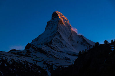 Low angle view of snowcapped mountains against clear blue sky