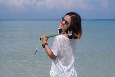 Young woman holding monopod while standing at beach