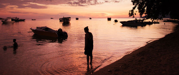 Silhouette people on sea against sky during sunset