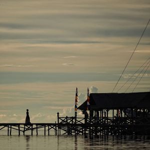 Silhouette woman on pier over sea against sky during sunset