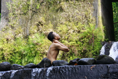 Side view of shirtless boy on rock