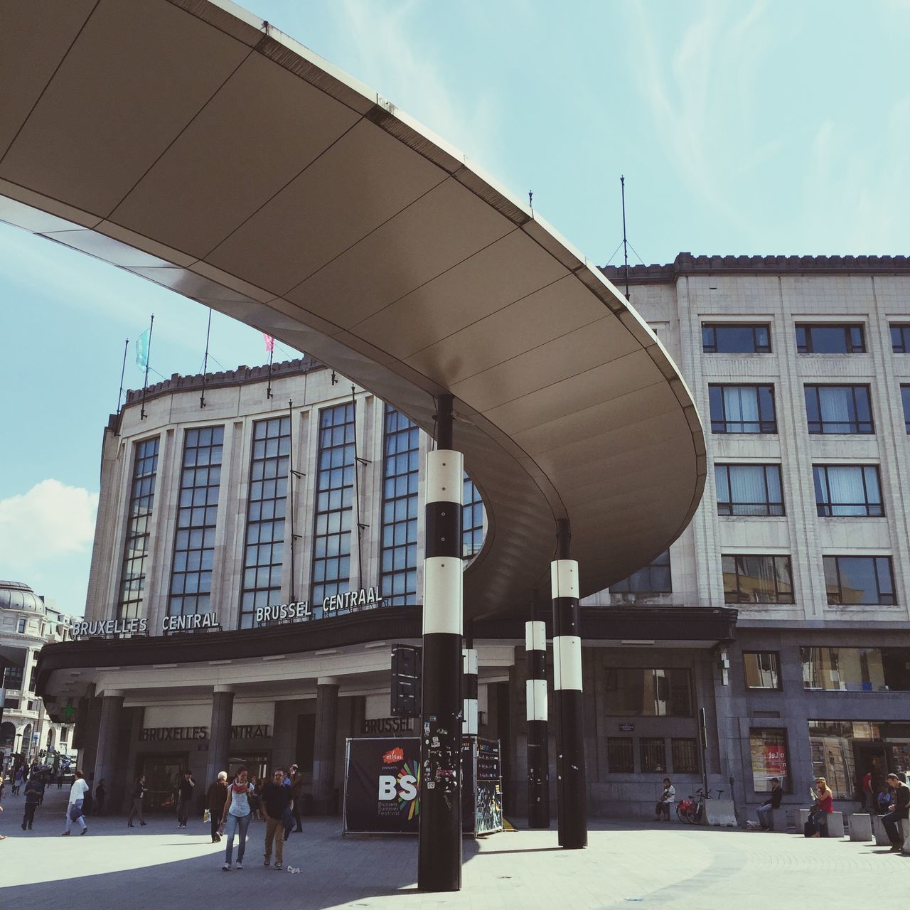 architecture, built structure, building exterior, sky, city, street, large group of people, sunlight, incidental people, building, city life, day, cloud, men, cloud - sky, low angle view, outdoors, walking, architectural column