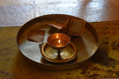 Close-up of illuminated diya by paper currency in plate on table