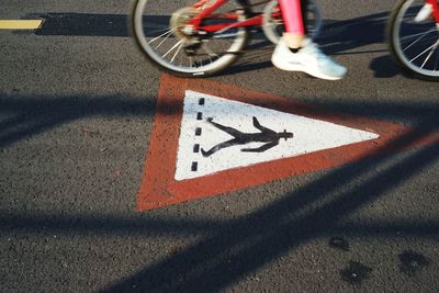 Low section of person cycling by pedestrian crossing sign on road