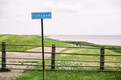 Road sign by sea against sky