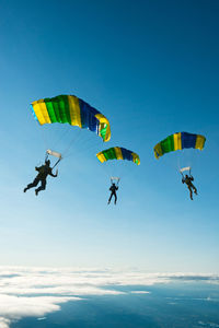 Low angle view of people paragliding against sky