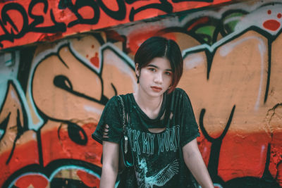 Portrait of young woman standing against graffiti wall