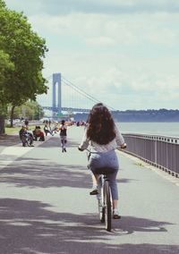 Rear view of women with bicycle on bridge in city