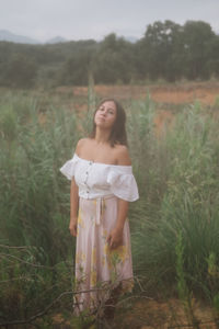 Portrait of young woman standing amidst plants against sky in forest