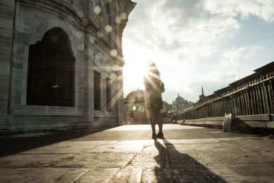 Woman walking by buildings in city against sky 