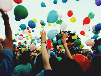 Crowd throwing colorful balloons against sky during festival