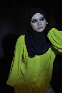 Portrait of young woman standing against black background