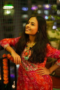 Young woman smiling while standing against illuminated wall