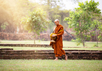 Full length of monk walking on grassy field at park