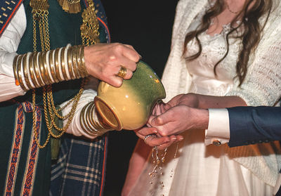 Midsection of man pouring water on bride and groom hands during wedding