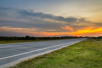 Road by field against sky during sunset