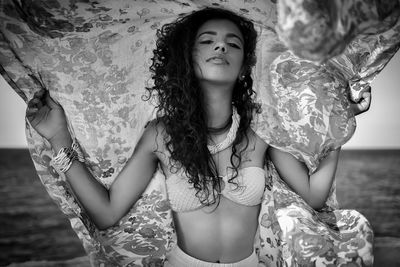 Portrait of sensuous young woman holding scarf at beach