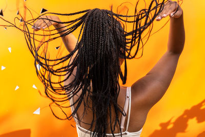 Back view of unrecognizable african american female throwing long braided hair on vivid yellow background in barcelona