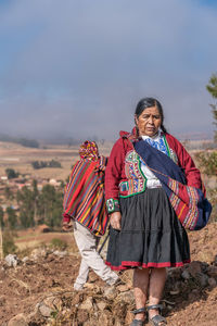 Senior peruvian female farmer in traditional costume standing in rural field in sunny day in chinchero