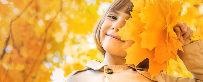 Portrait of girl holding maple leaves in forest