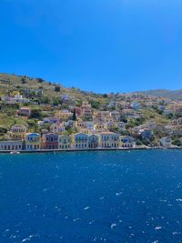 Buildings by sea against clear blue sky