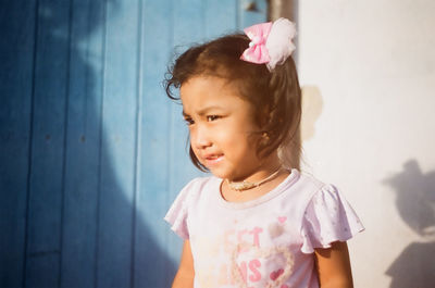 Cute girl looking away while standing against wall