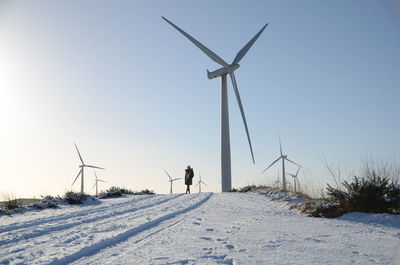 Wind turbines on snowed landscape against clear sky