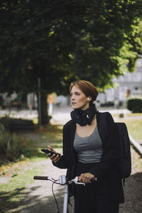 Female commuter with smart phone and bicycle walking in park