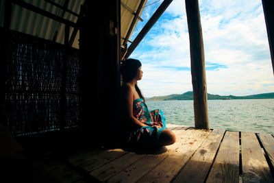 Rear view of young woman sitting in meditation on the porch of a bungalow overlooking the sea