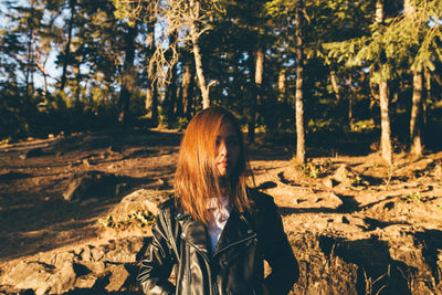 Young woman wearing leather jacket against trees during sunset