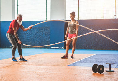 Woman looking at instructor exercising with rope in gym