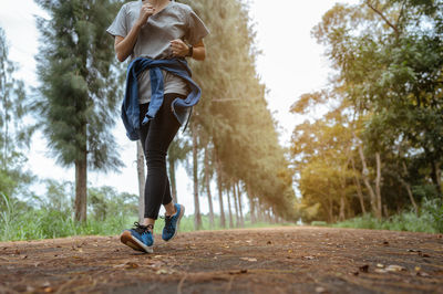 Low section of woman running on footpath amidst trees