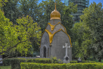 Low angle view of cross amidst trees and building