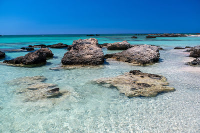 Rocks on shore against clear blue sky