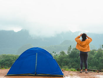 Woman camping blue tent on mountain peak and enjoying beautiful nature of hills