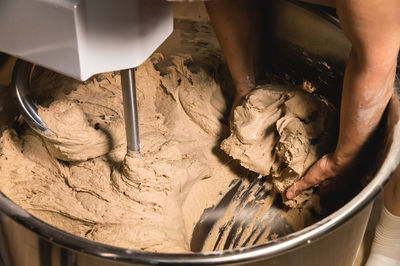 Close-up of baker's female hands holding dough against the background of a production dough mixer in