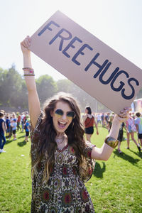 Portrait of cheerful young woman holding text on cardboard during sunny day