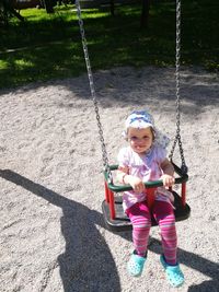 Full length of smiling girl sitting on swing at park