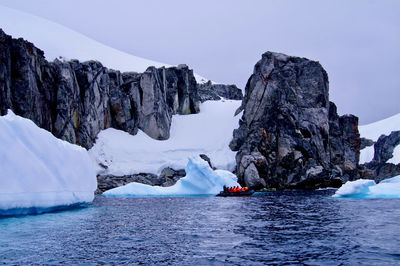 Adventurers on a zodiac closely exploring the icebergs and rocky formations in antarctica.