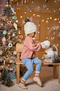 Full length of cute girl playing with christmas tree at home