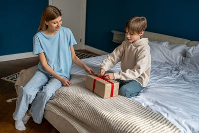 Boy using mobile phone while sitting on bed at home