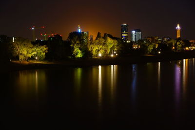 Illuminated buildings by river against sky at night