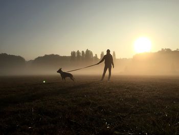 Woman standing with dog on field during sunrise