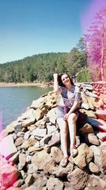 Portrait of smiling young woman standing on rock against lake
