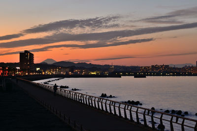 Silhouette bridge over sea against sky during sunset